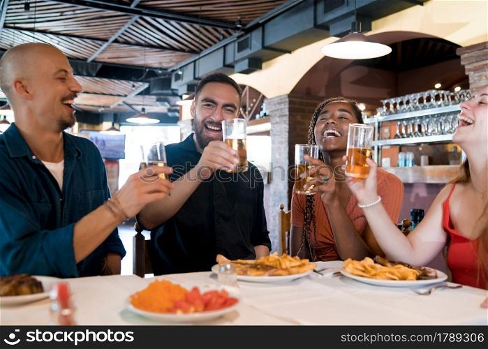 Group of diverse friends drinking beer while enjoying a meal together in a restaurant. Friends concept.