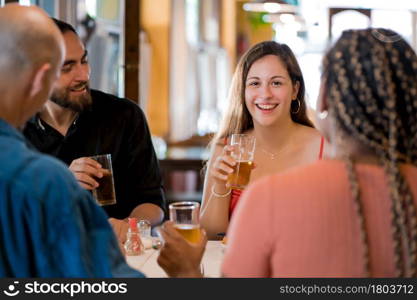 Group of diverse friends drinking beer while enjoying a meal together in a restaurant. Friends concept.