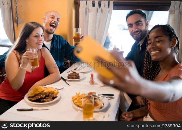 Group of diverse friends taking a selfie with a mobile phone while enjoying a meal together in a restaurant. Friends concept.