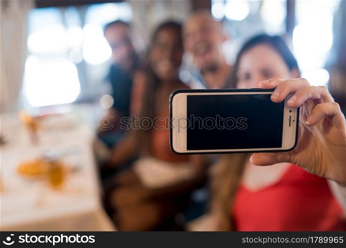 Group of diverse friends taking a selfie with a mobile phone while enjoying a meal together in a restaurant. Friends concept.