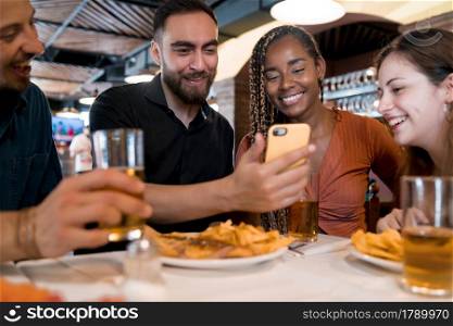 Group of diverse friends using a mobile phone while enjoying a meal together in a restaurant. Friends concept.