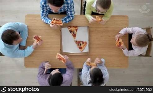 Group of diverse people eating pizza sitting around the table