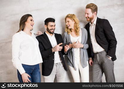 Group of elegant businesspeople standing against the wall and using their mobile phones