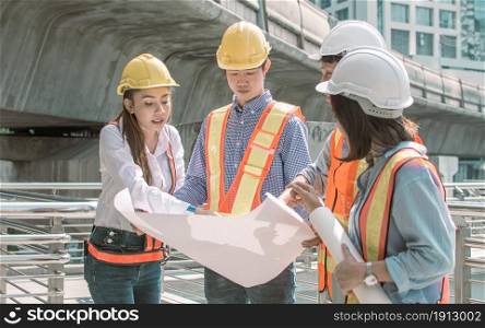 Group of engineer wearing safety helmets, looking to a drawing in paper and discussing about their construction project outside