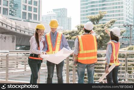 Group of engineer wearing safety helmets, looking to a drawing in paper and discussing about their construction project outside