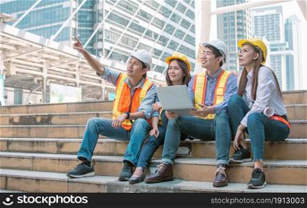 Group of engineer wearing safety helmets, pointing out, holding laptop and discussing about their construction project outside