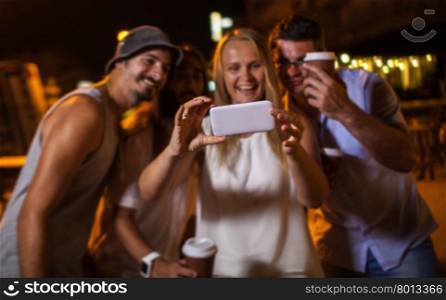 Group of excited friends taking selfie with smartphone at night. Focus on the mobile . Happy friends making phone selfie at night
