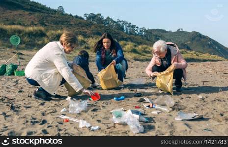 Group of female volunteers picking up trash on the beach. Female volunteers cleaning the beach