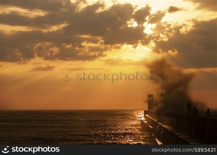 Group of fishermen on the pier near lighthouse with wave splash at sunset, Porto, Portugal