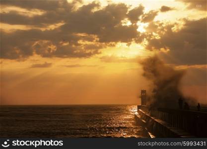 Group of fishermen on the pier near lighthouse with wave splash at sunset, Porto, Portugal