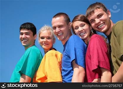 Group of five friends in multicolor shirts on sky background