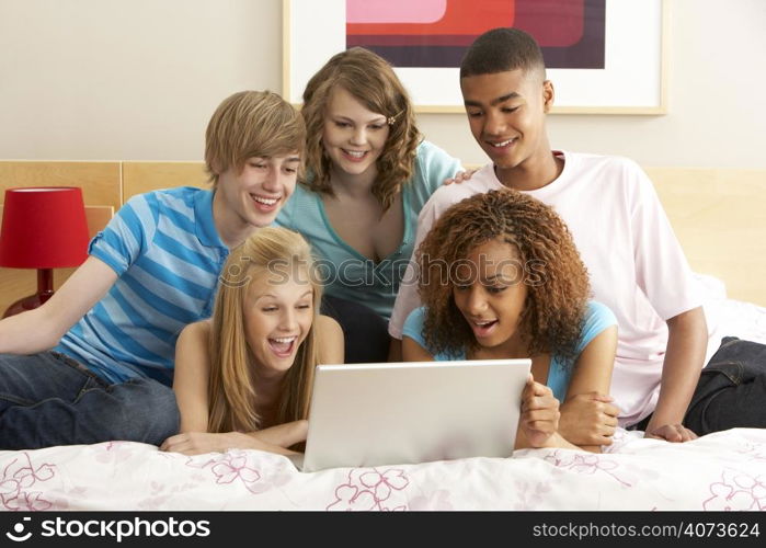 Group Of Five Teenage Using Laptop In Bedroom