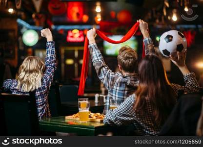 Group of football fans with scarf and ball watching match and drinks beer in sports bar. Tv broadcasting, young friends leisures in pub, favorite team wins. Group of football fans watching match in sport bar