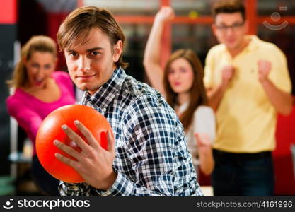 Group of four friends in a bowling alley having fun, three of them cheering the one in charge to throw the bowling ball