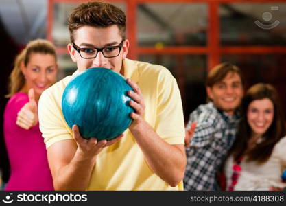 Group of four friends in a bowling alley having fun, three of them cheering the one in charge to throw the bowling ball