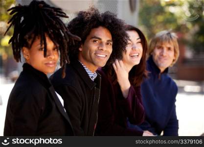 Group of four people of different ethnicities sitting in a row. Horizontally framed shot.