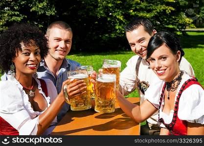 Group of four people - two Couples - in traditional Bavarian dress, Lederhosen and Dirndl, in a beer garden