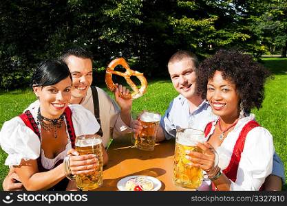 Group of four people - two Couples - in traditional Bavarian dress, Lederhosen and Dirndl, in a beer garden with Pretzel and Obatzter (traditional cheese)