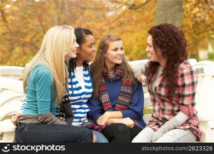 Group Of Four Teenage Girls Sitting And Chatting On Bench In Autumn Park