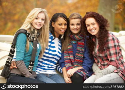 Group Of Four Teenage Girls Sitting On Bench In Autumn Park