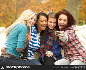 Group Of Four Teenage Girls Taking Picture With Camera Sitting On Bench In Autumn Park