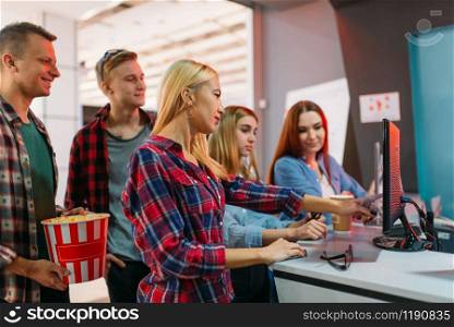 Group of friends choosing movie in cinema box office. Male and female youth waiting in movie theater, entertainment lifestyle. Friends choosing movie in cinema box office