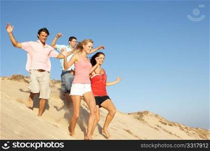 Group Of Friends Enjoying Beach Holiday Running Down Dunes