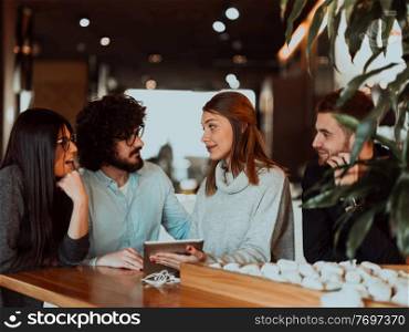 Group of friends hanging out in a coffee shop with a laptop amongst them. Happy young people sitting at restaurants using a laptop. A group of friends hanging out in a cafe, and talking about business