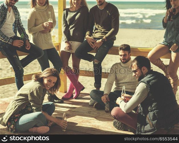Group of friends having fun on autumn day at beach. Happy Group Of Friends Hanging Out At Beach House having fun and drinking beer on autumn day colored filter