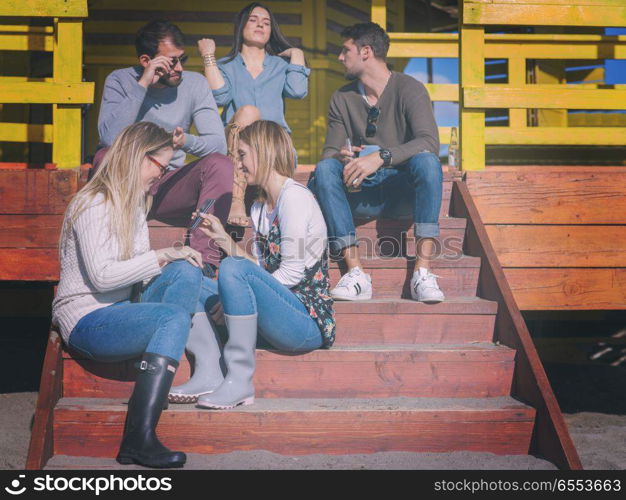 Group of friends having fun on autumn day at beach. Happy Group Of Friends Hanging Out At Beach House having fun and drinking beer on autumn day colored filter