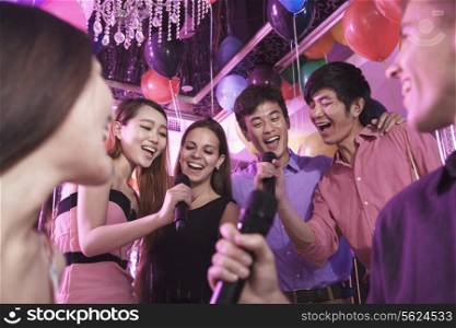 Group of friends holding microphones in a nightclub and singing together karaoke