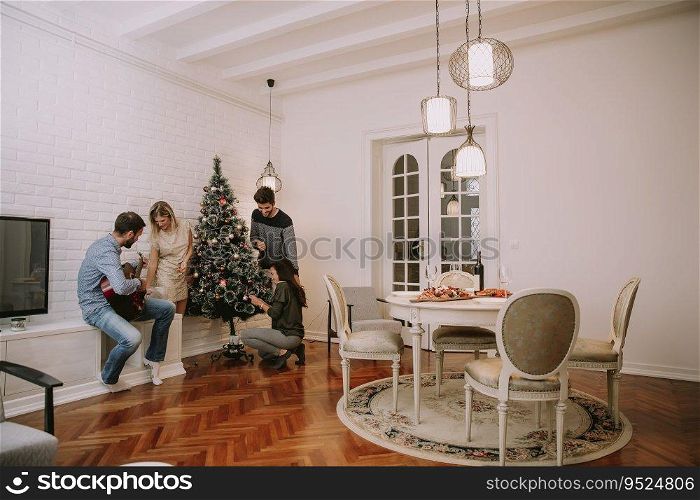Group of friends in  the living room next to a Christmas tree having fun and playing guitar