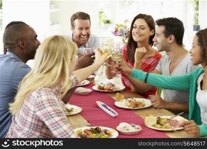 Group Of Friends Making Toast Around Table At Dinner Party