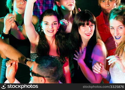 Group of friends - men and women of different ethnicity - dancing to the music in a disco club having lots of fun