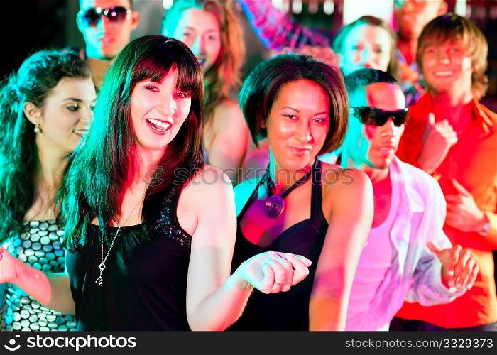 Group of friends - men and women of different ethnicity - dancing to the music in a disco club having lots of fun