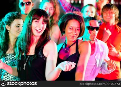 Group of friends - men and women of different ethnicity - dancing to the music in a disco club having lots of fun