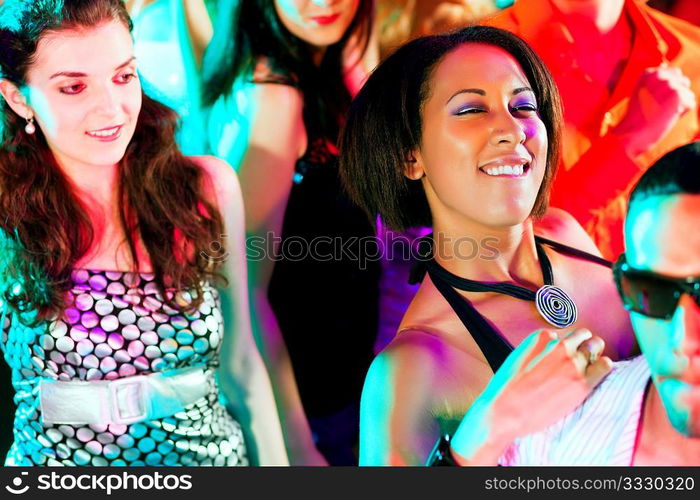 Group of friends - men and women of different ethnicity - dancing to the music in a disco club having lots of fun