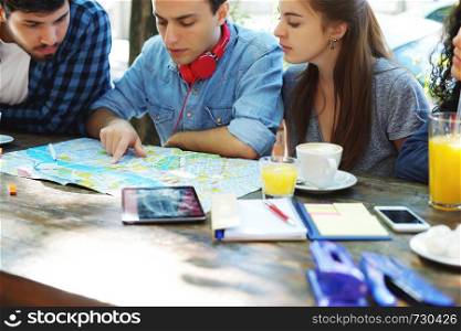 Group of friends planing a trip and looking at a map at a coffee. Travel concept.
