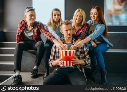 Group of friends poses with popcorn in cinema hall before the showtime. Male and female youth waiting in movie theater, entertainment lifestyle