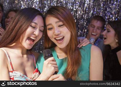 Group of friends singing into a microphone at karaoke