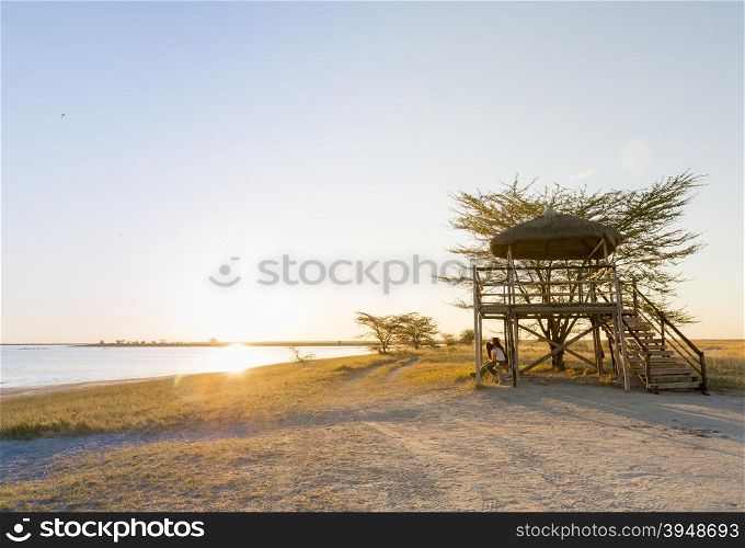 Group of friends sit relaxing at sunset on the beach under a large open air hut in Africa