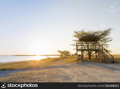 Group of friends sit relaxing at sunset on the beach under a large open air hut in Africa