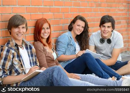 Group of friends students sitting in row against brick wall