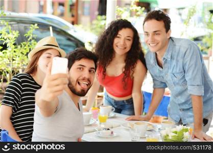 Group of friends taking selfie on a mobile phone in a coffee shop. People having fun together, friendship concept.