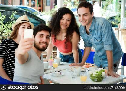 Group of friends taking selfie on a mobile phone in a coffee shop. People having fun together, friendship concept.