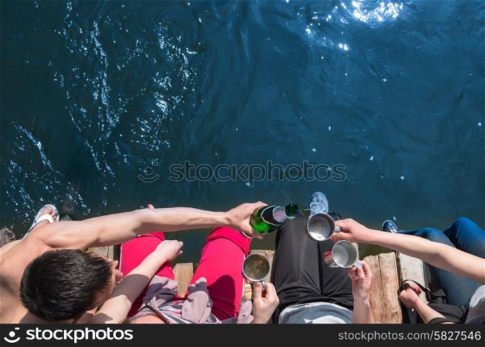 Group of friends toasting drinks and having party on a wooden bridge at the sea