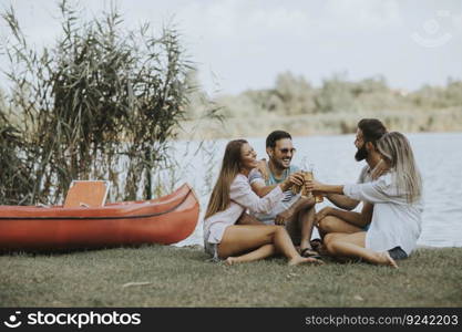 Group of friends with cider bottles sitting by the boat near the beautiful lake and having fun on a summer day