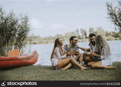 Group of friends with cider bottles sitting by the boat near the beautiful lake and having fun on a summer day