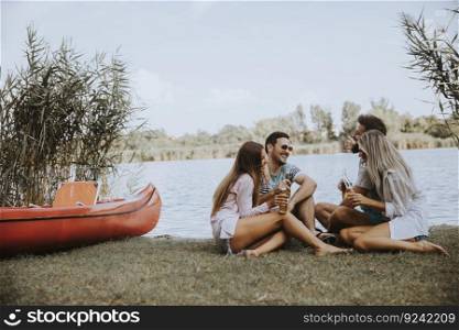 Group of friends with cider bottles sitting by the boat near the beautiful lake and having fun on a summer day
