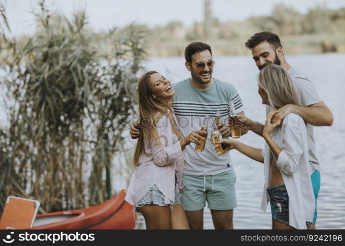 Group of friends with cider bottles standing by the boat near the beautiful lake and having fun on a summer day